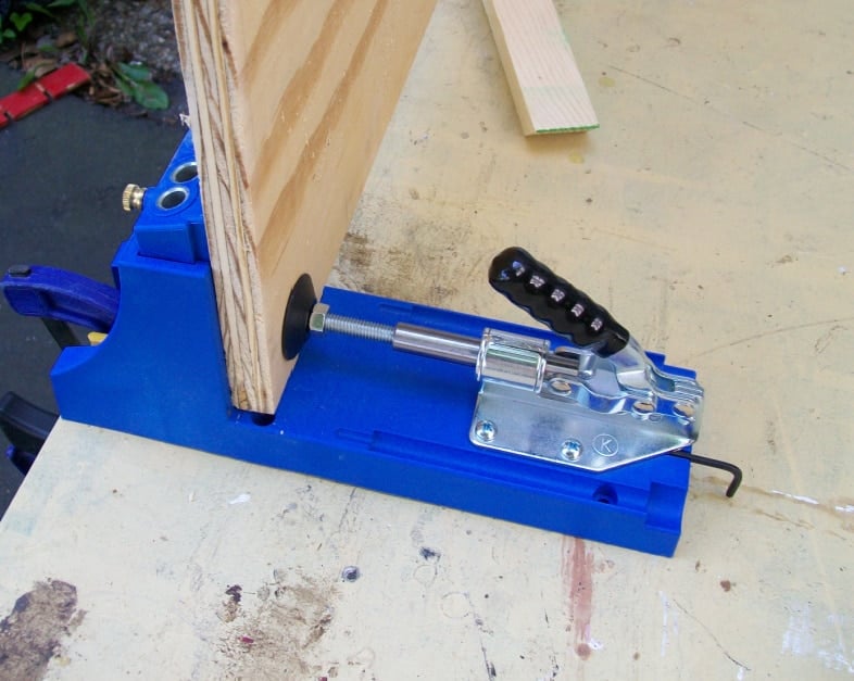 plywood resting in a blue kreg jig ready to drill a pocket hole