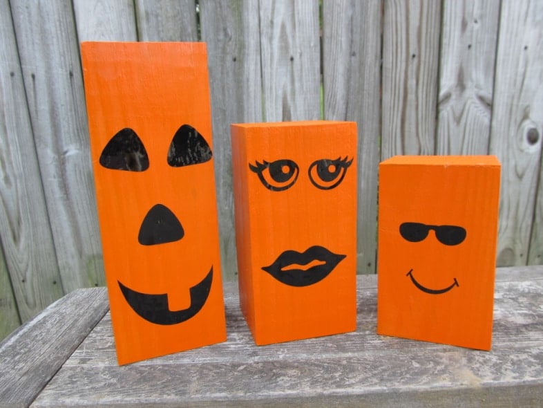 three orange wooden post jack-o-lanterns of varying sizes