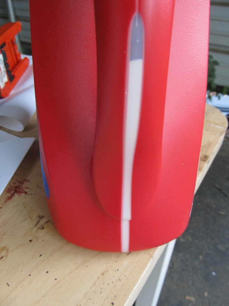 red laundry jug with paint showing through the window of the jug