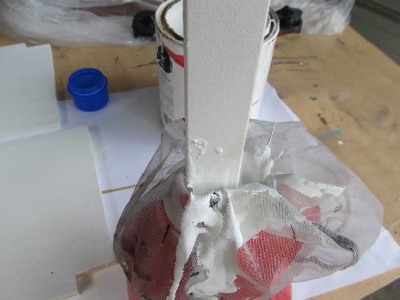 paint stick pushing mesh strainer into laundry jug