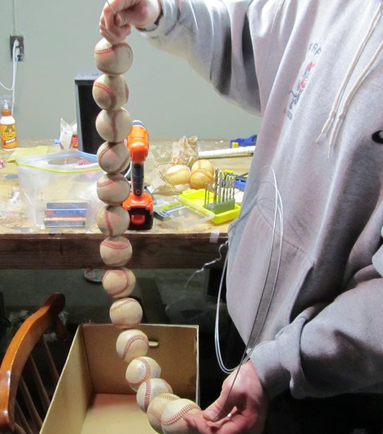 man holding a wire with many baseballs