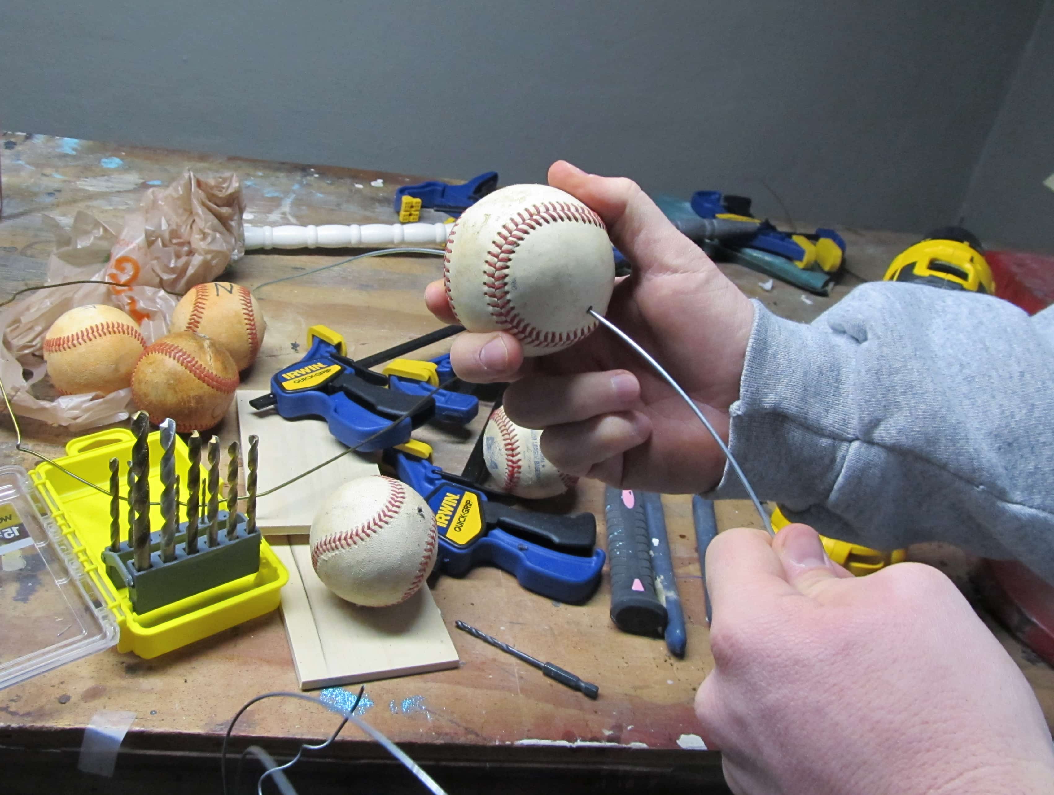 man pushing wire through a hole in a baseball