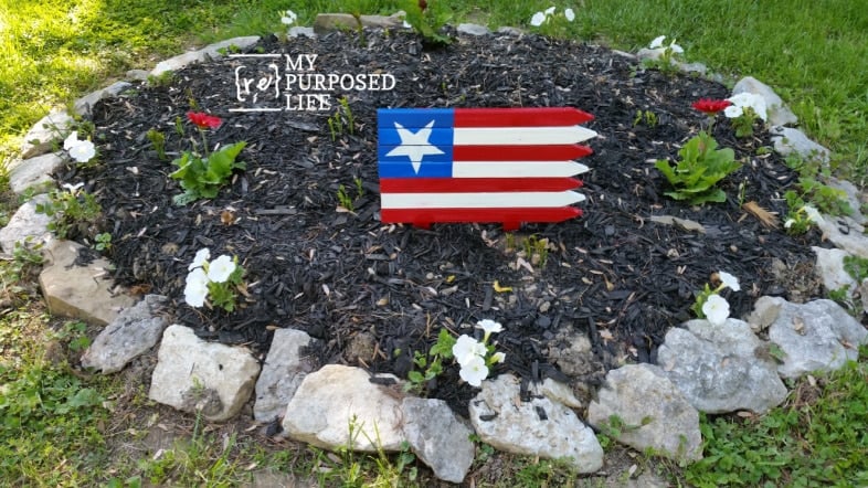 americana garden stake flag in a creek rock flower bed