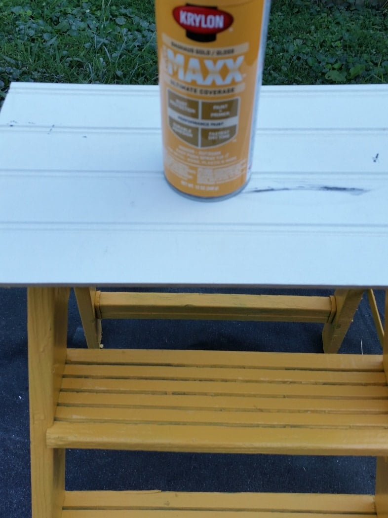 yellow spraypaint can resting on large board on top of a stepladder