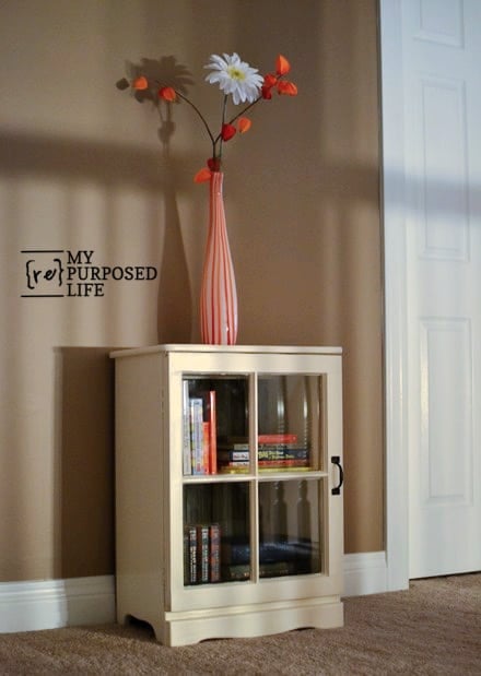 window cupboard with books behind door and a vase of flowers on top MyRepurposedLife