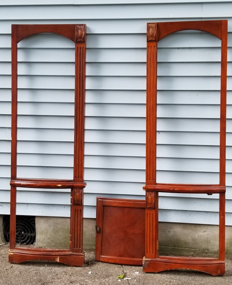 two tall brown stained armoire doors leaning against a house