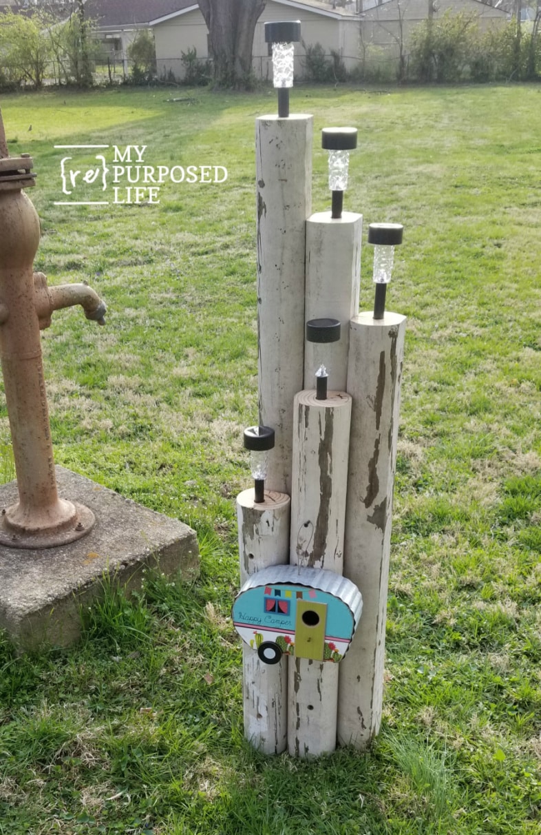 landscape timber solar lights in the yard by an antique water pump and a happy camper birdhouse hanging from it