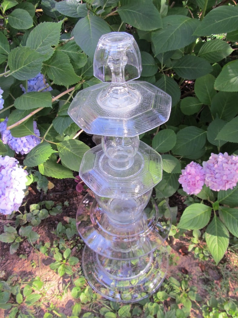 tall glass garden totem sitting in front of a bush