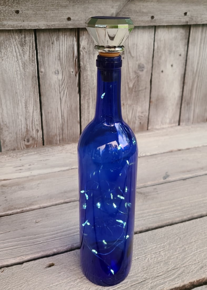 wine bottle with solar lights resting on wooden bar