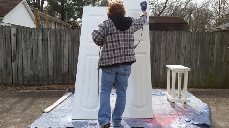 woman using a paint sprayer to paint closet doors outside