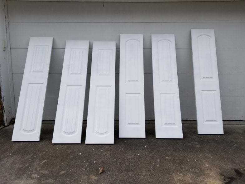 six closet doors leaning against garage after being painted