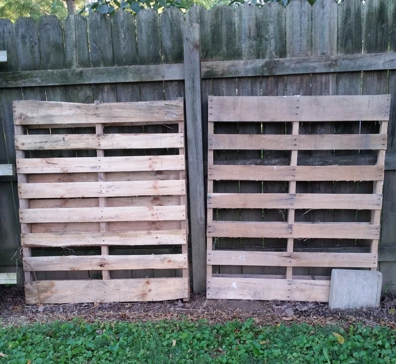 two free pallets leaning against a wooden fence