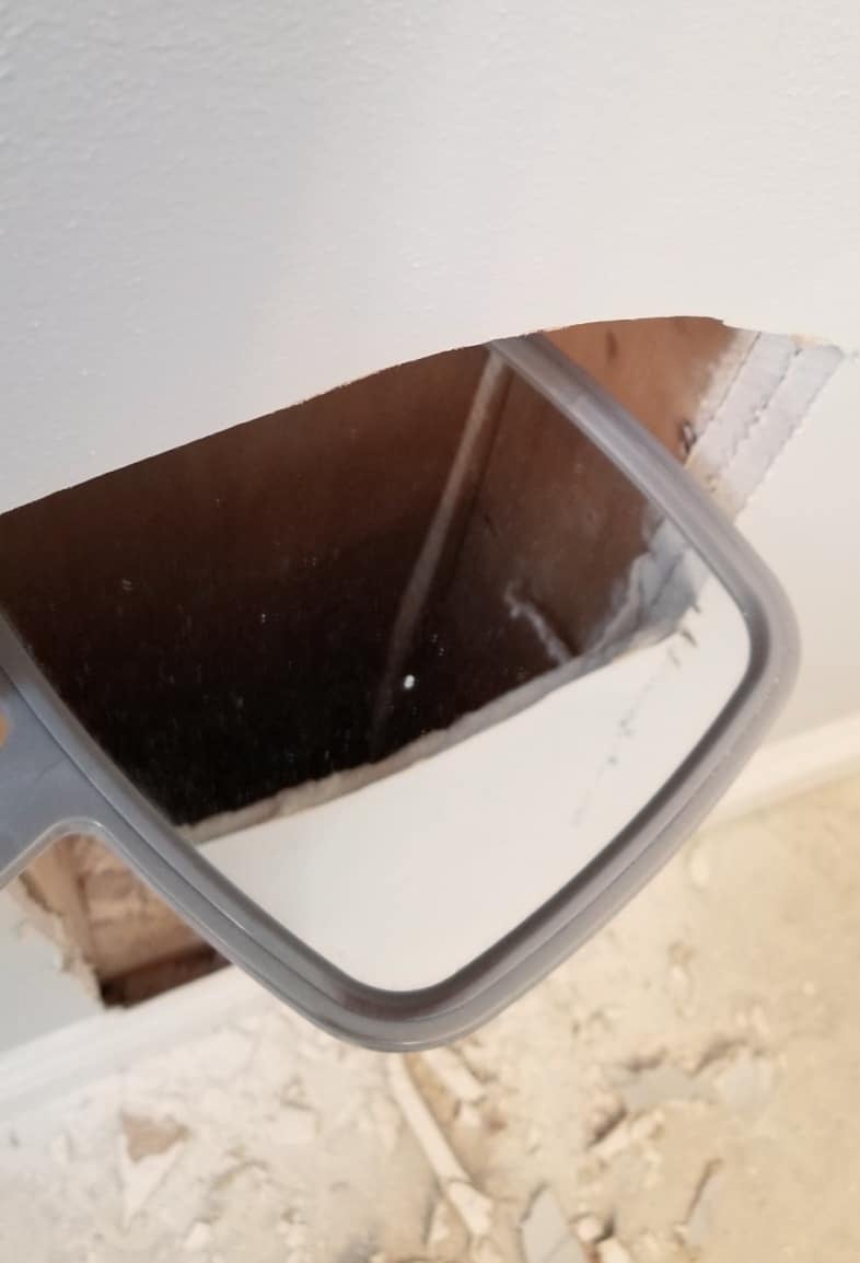 a hand mirror halfway inside the wall to reflect the interior of the wall space