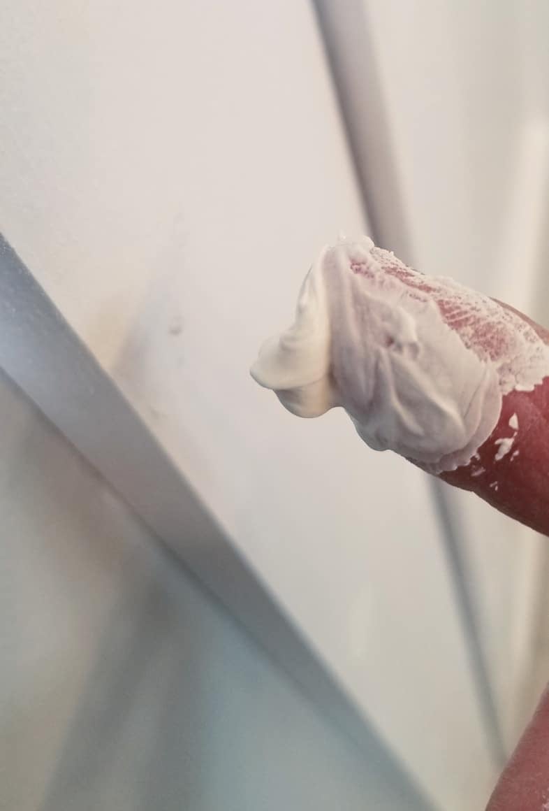 patching nail holes with drywall mud on her finger