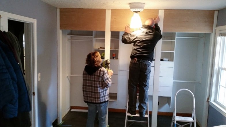 man and woman installing a plywood header at the top of a wall to wall closet