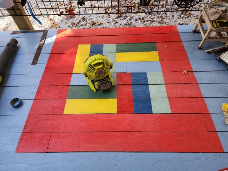 a battery operated fan drying paint on a square painted porch rug