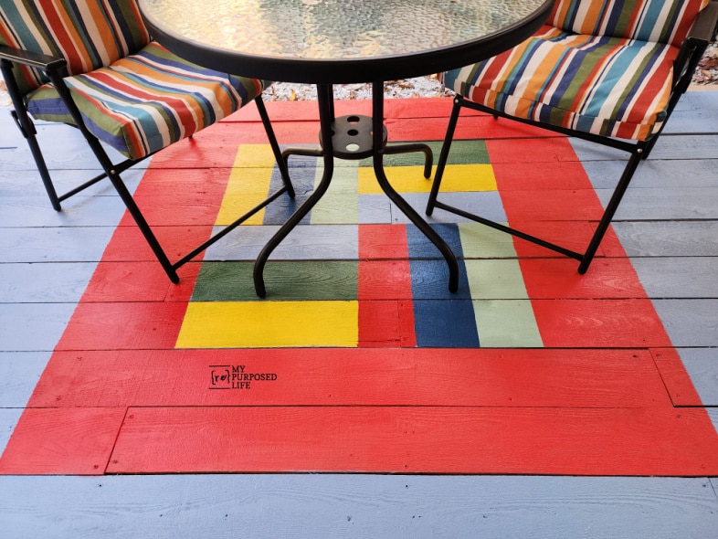 small table and chairs resting on a square painted porch rug