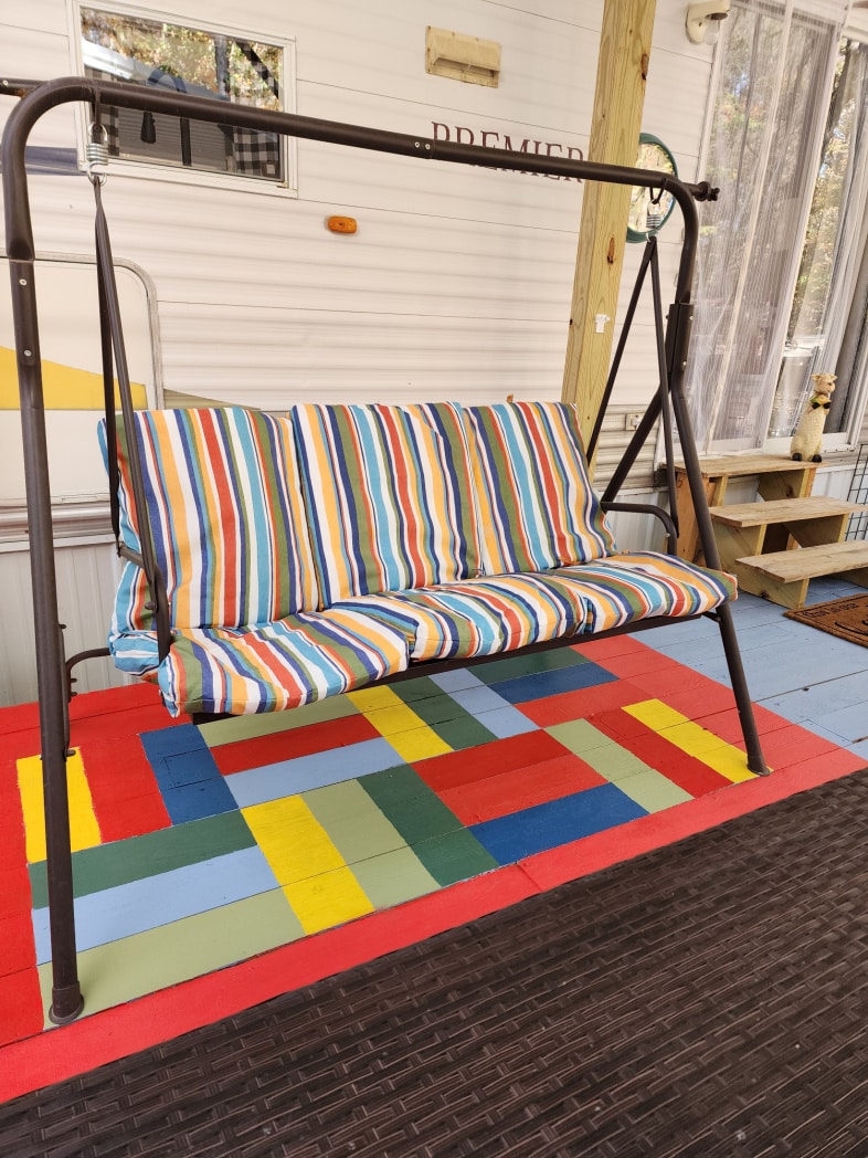 porch swing with colorful striped cushions on painted porch rug