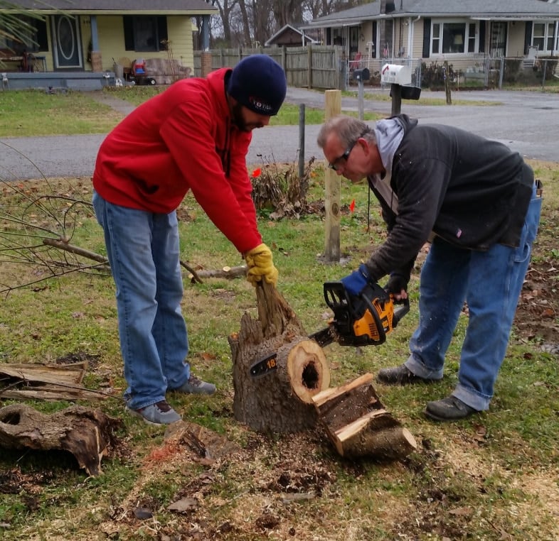 two men cutting a stump with a chain saw