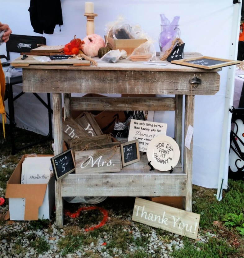 outdoor bar at craft show with items displayed on top and shelves