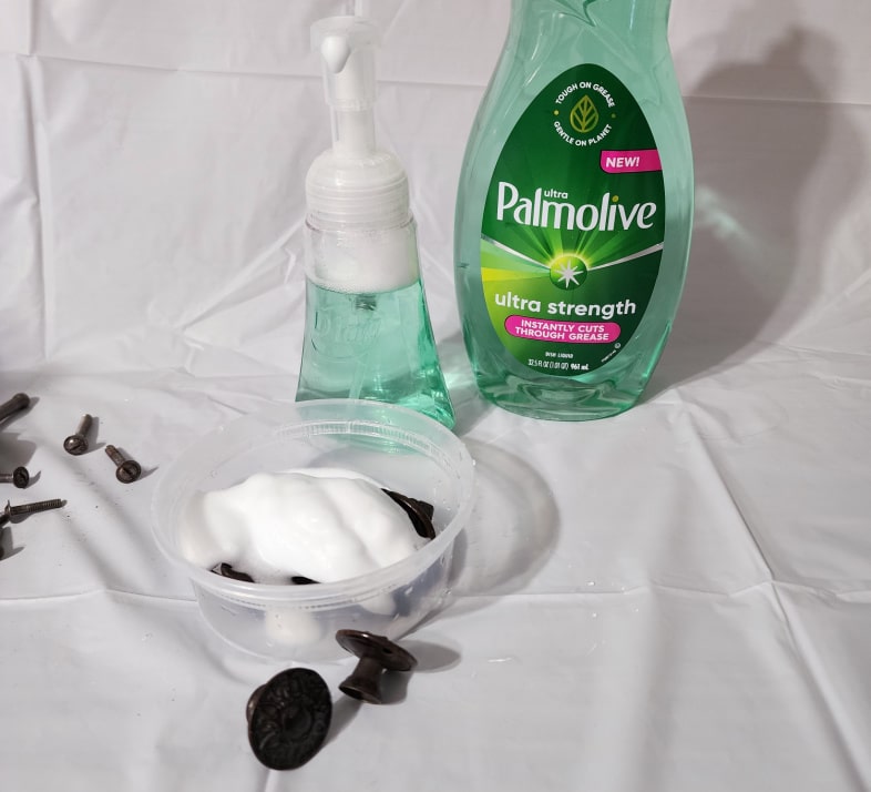 foam dish soap soaking hardware in a plastic containter