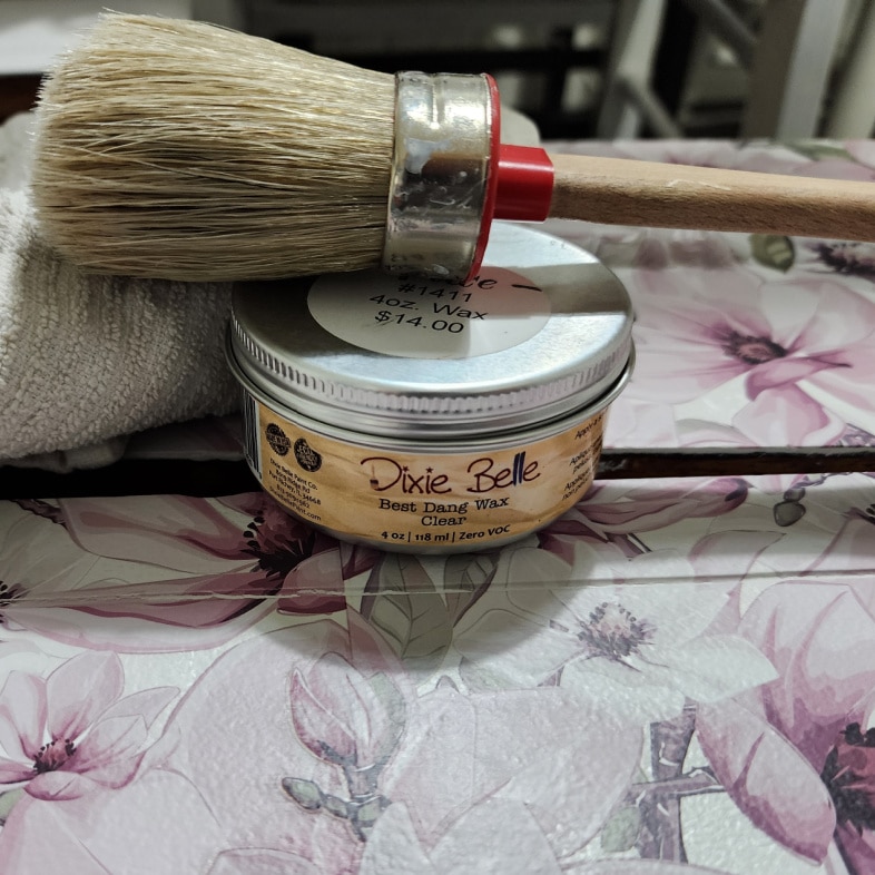 a jar of wax, a paintbrush and a rag resting on top of dresser drawer with furniture transfer