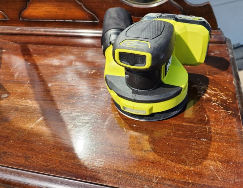 ryobi orbital sander resting on a damaged dresser top