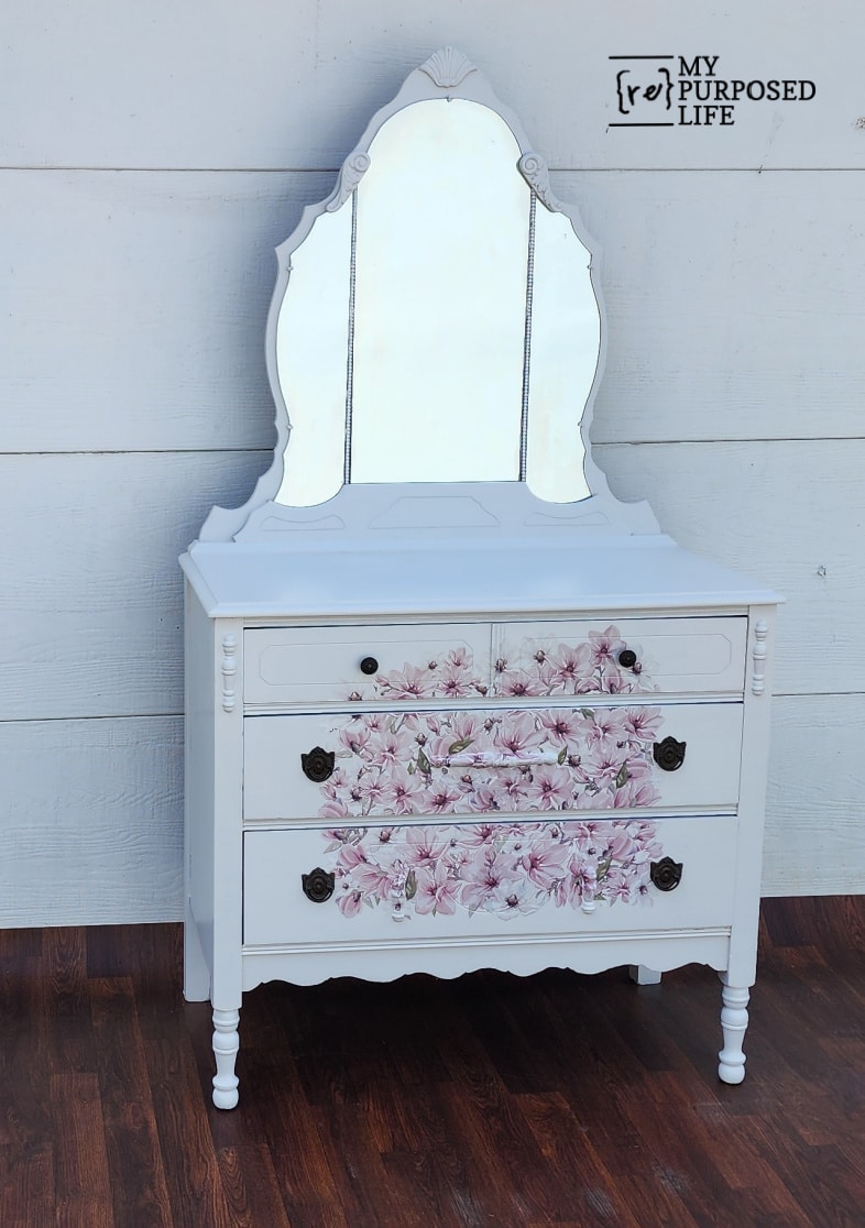 light gray antique dresser with triple mirror and pink magnolia flowers on the front drawers