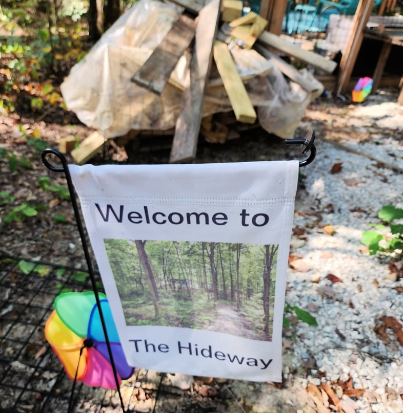 garden flag reading welcome to the hideaway with a pile of scrap wood