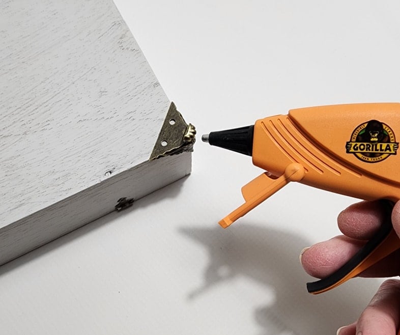 gorilla glue gun attaches small metal feet to bottom of painted wooden box