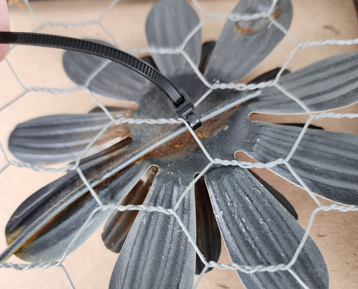 closeup image of the zip tie holding a metal flower onto the chicken wire