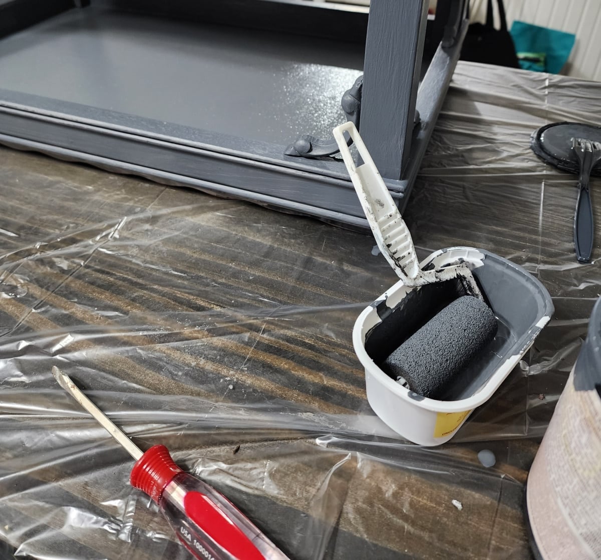 small foam paint roller in a plastic tub painting a side table dark gray